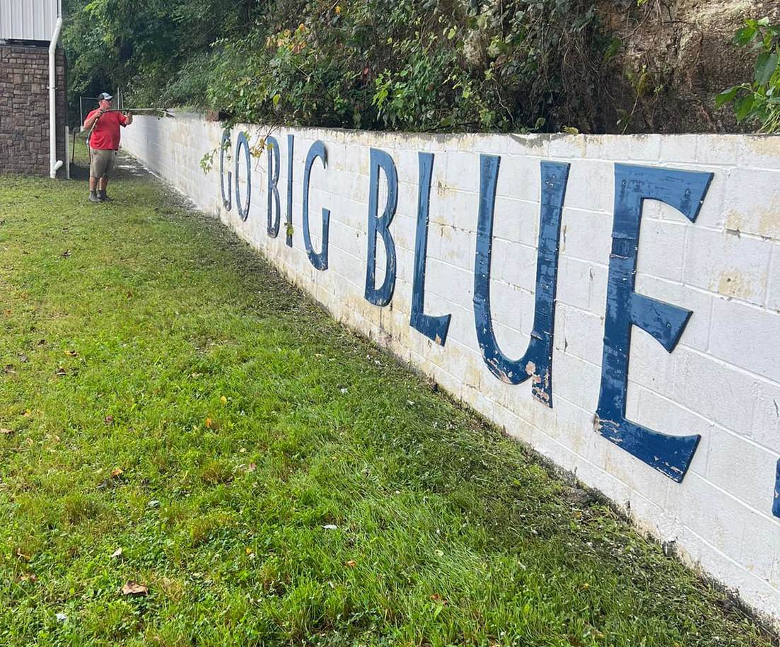 Washing a long concrete block retaining wall painted with school lettering