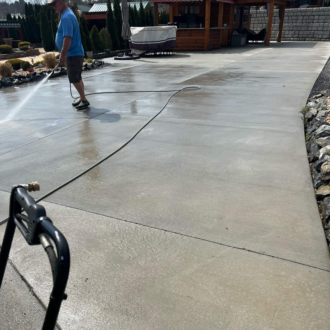 Surface cleaning a wide concrete apron with a wand, the hose running back across the wet slab