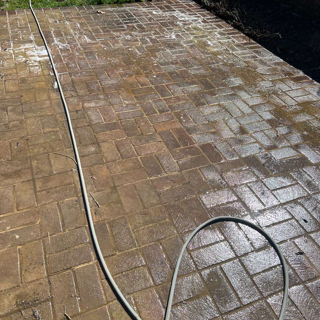 A tan brick paver walkway part way through the clean, the hose looped across it