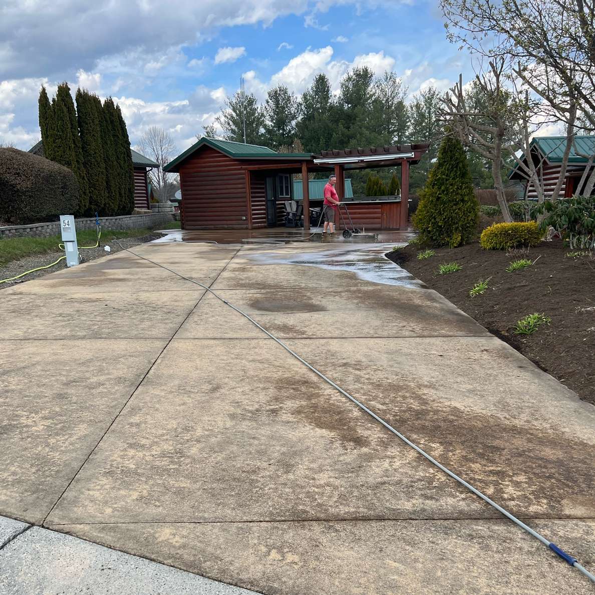 A log cabin and its concrete driveway photographed from the road, the drive part way through the clean
