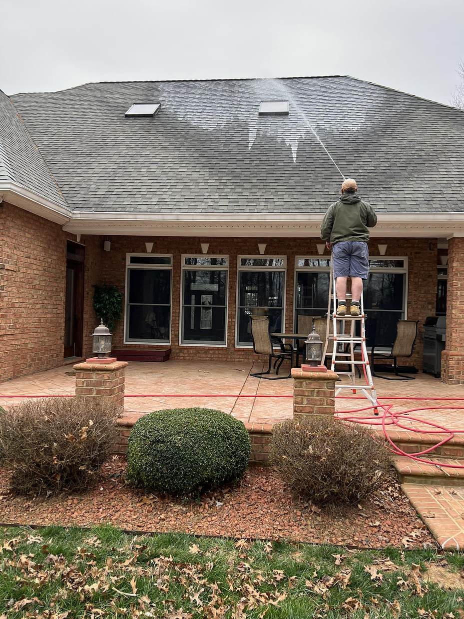 Soft washing the shingle roof of a brick ranch home from an extension ladder