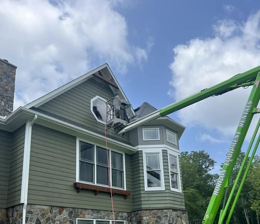 An articulating boom lift reaching over a two story house to wash the upper gable and roof