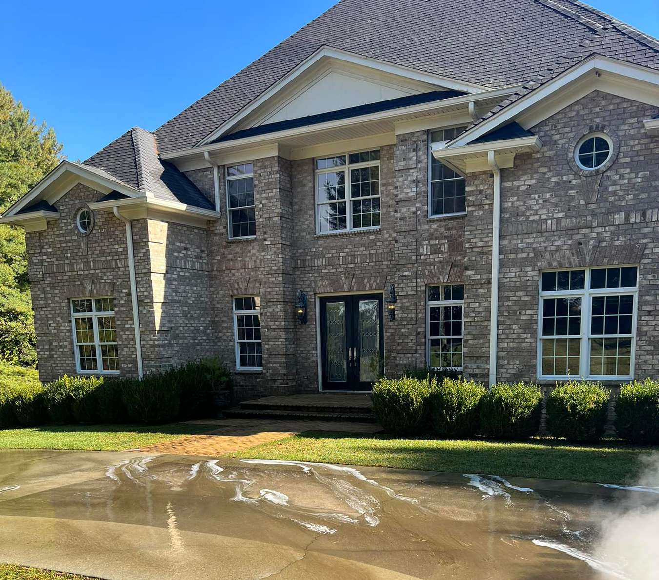 A large brick colonial with white portico columns, rinse water running across the front court