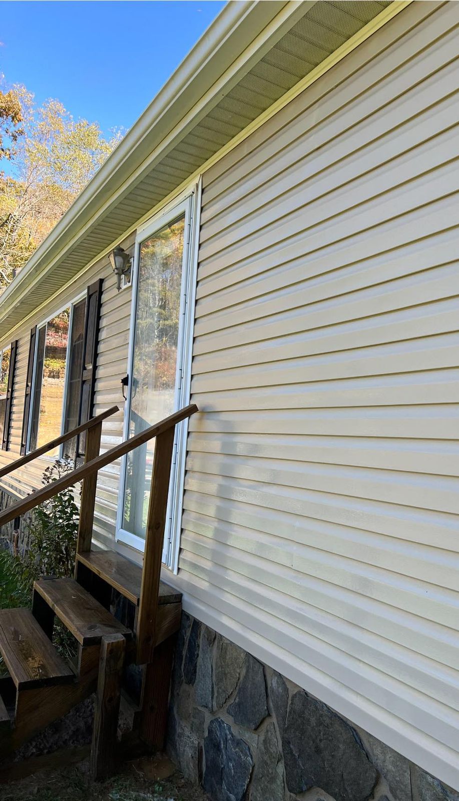 The same cream vinyl siding after the wash, clean above the stone skirt