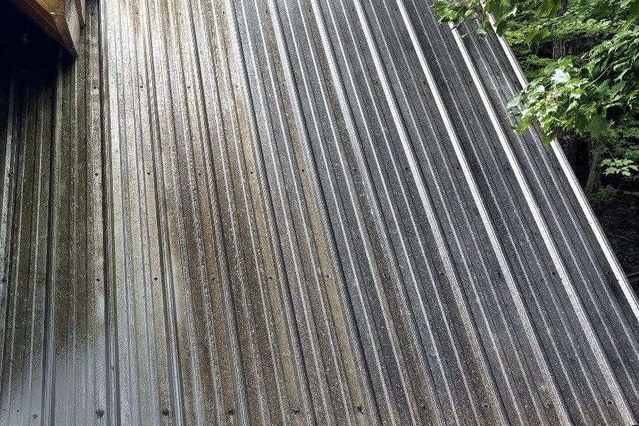 One metal roof photographed part way through the job, the washed panels running bright beside the stained ones